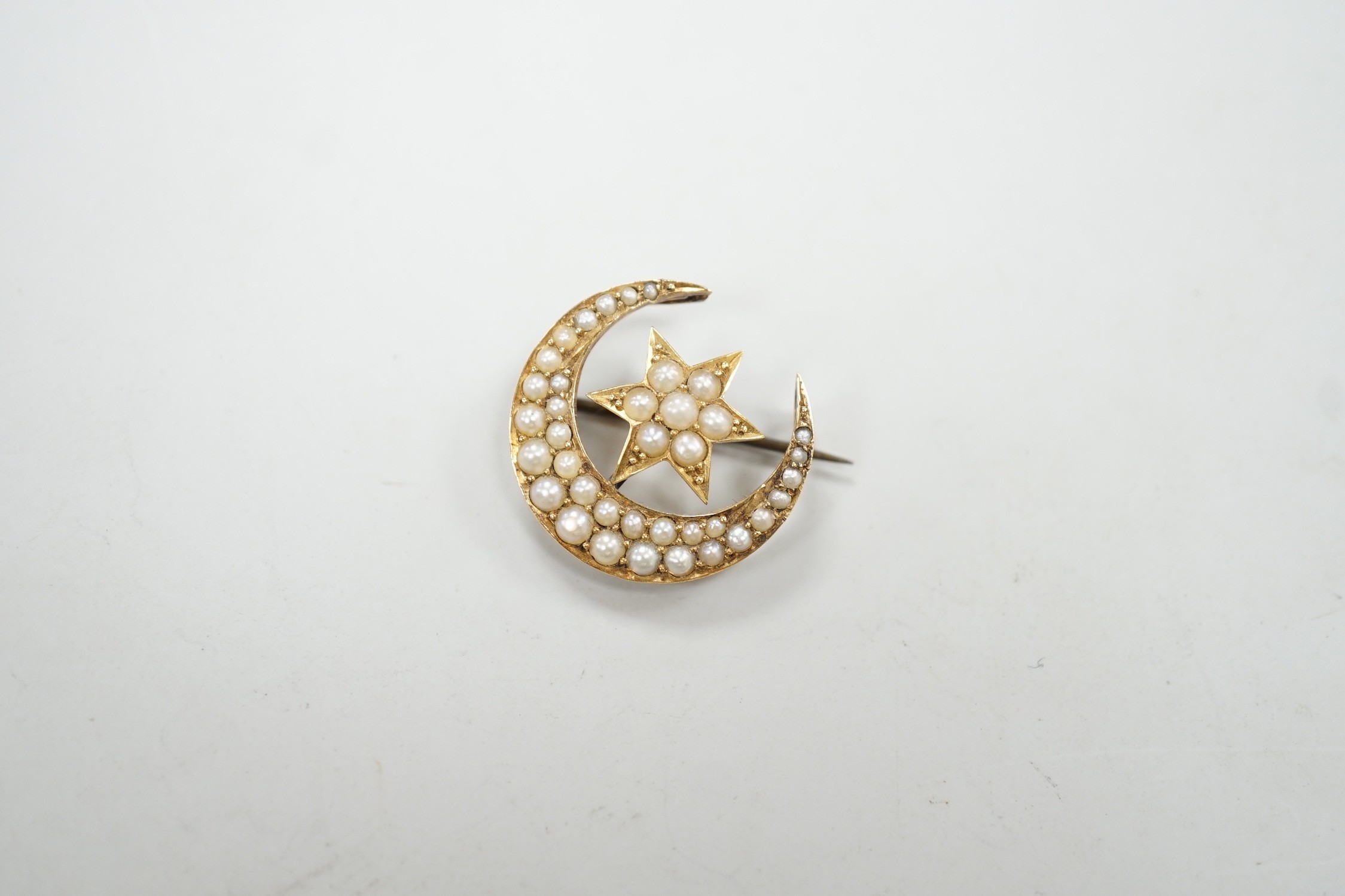 An Edwardian yellow metal and seed pearl set crescent moon and star brooch, 22mm, gross weight 4 grams.